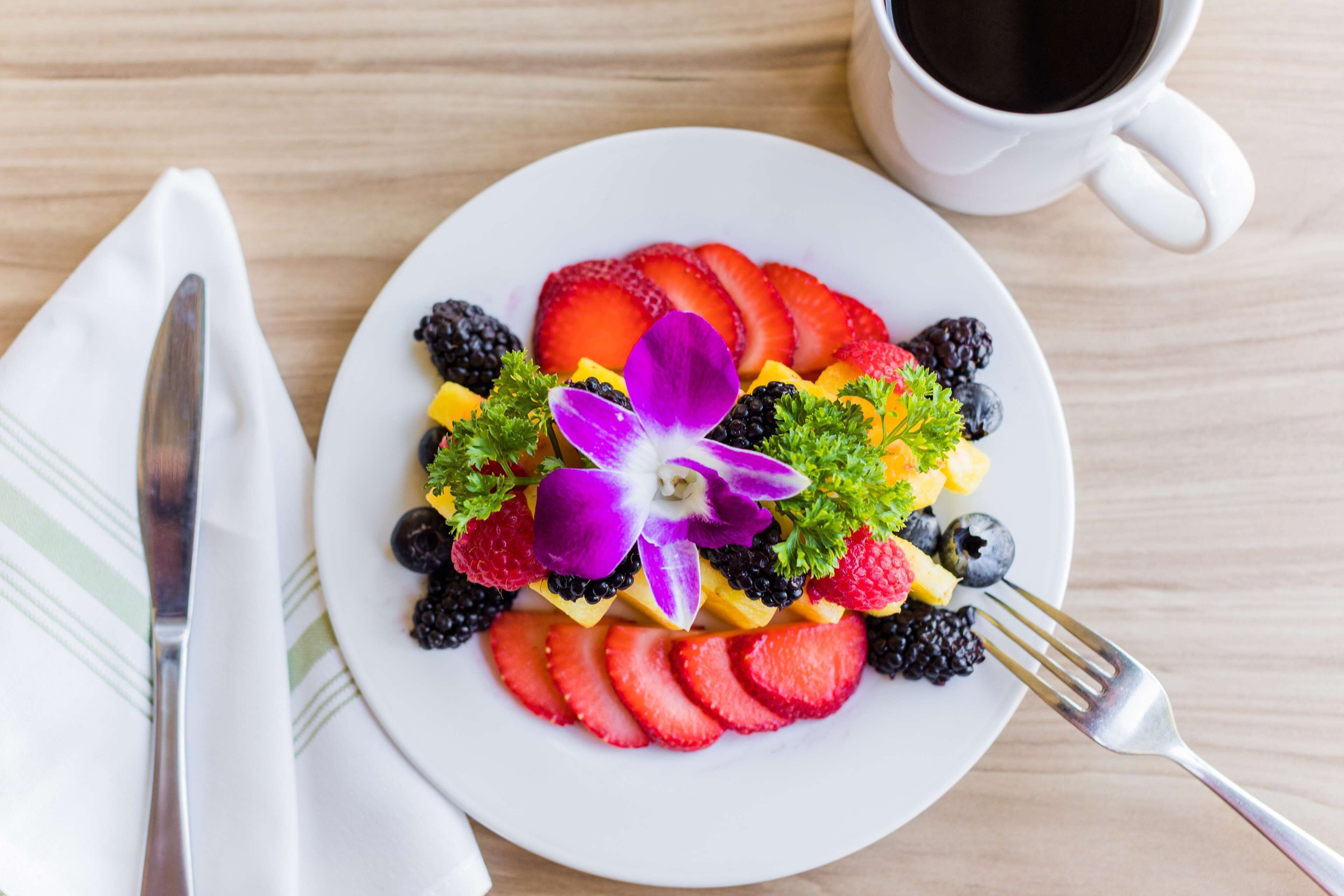 Un plato de frutas variadas sobre una mesa de madera, con una taza blanca y un tenedor.