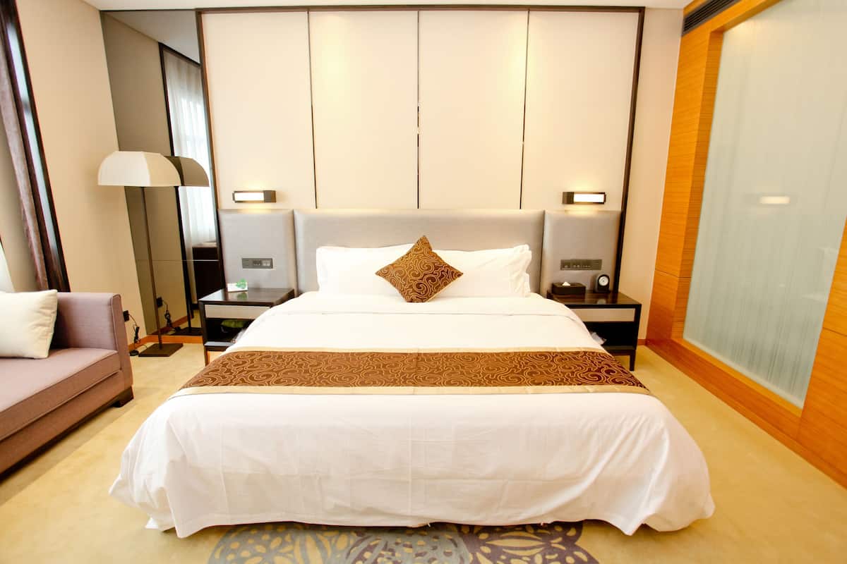 Une chambre d’hôtel bien aménagée, avec un grand lit, un canapé, une table de chevet avec une lampe et une grande fenêtre.