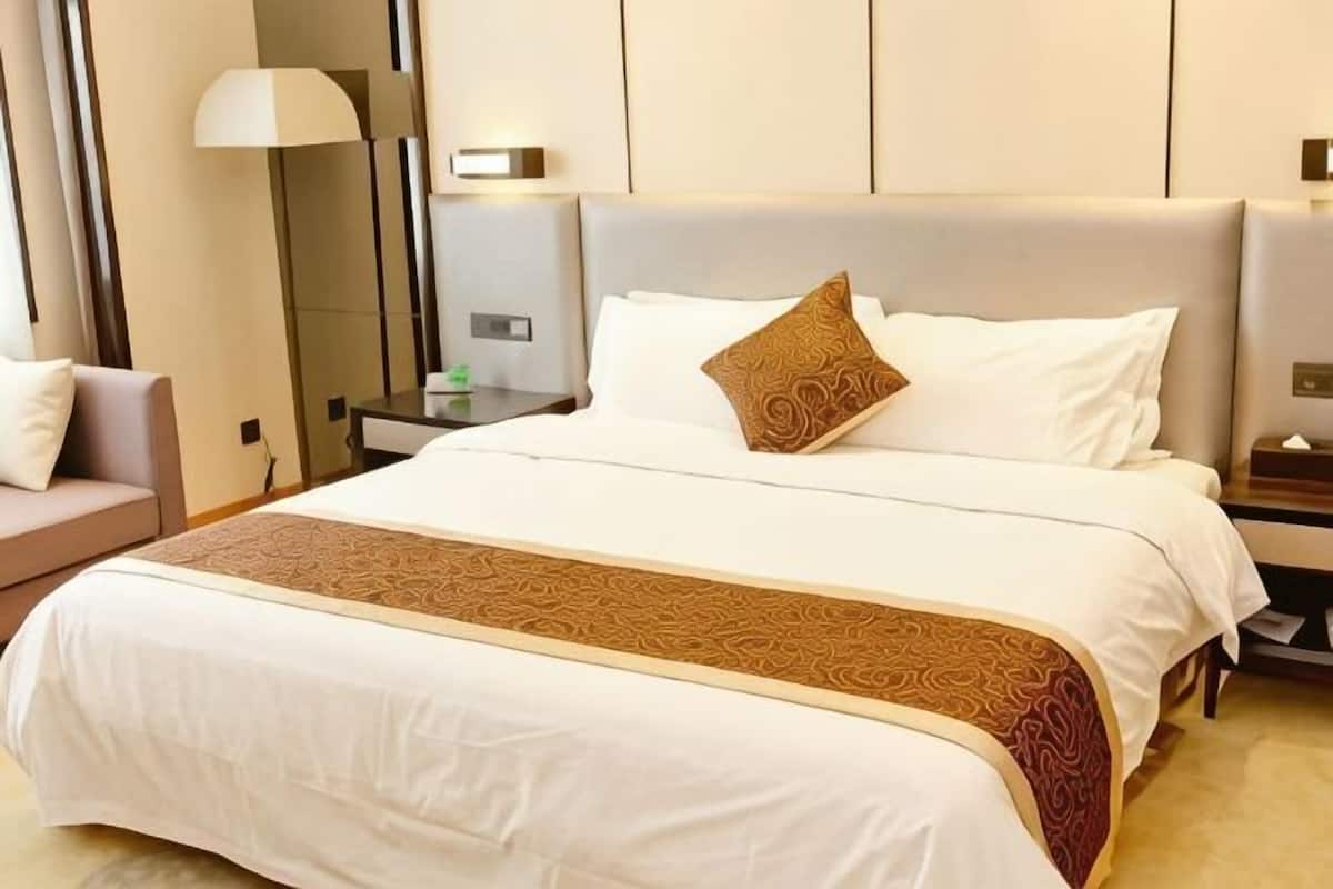 Une chambre d’hôtel avec un grand lit, une table de chevet, une lampe et une commode.