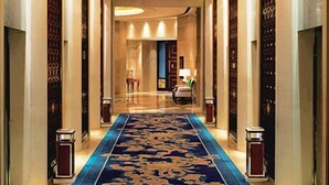 A hotel corridor with a blue carpet, chandeliers, and patterned walls. - Lamtin Longwin Hotel Wuhan (Wuhan)