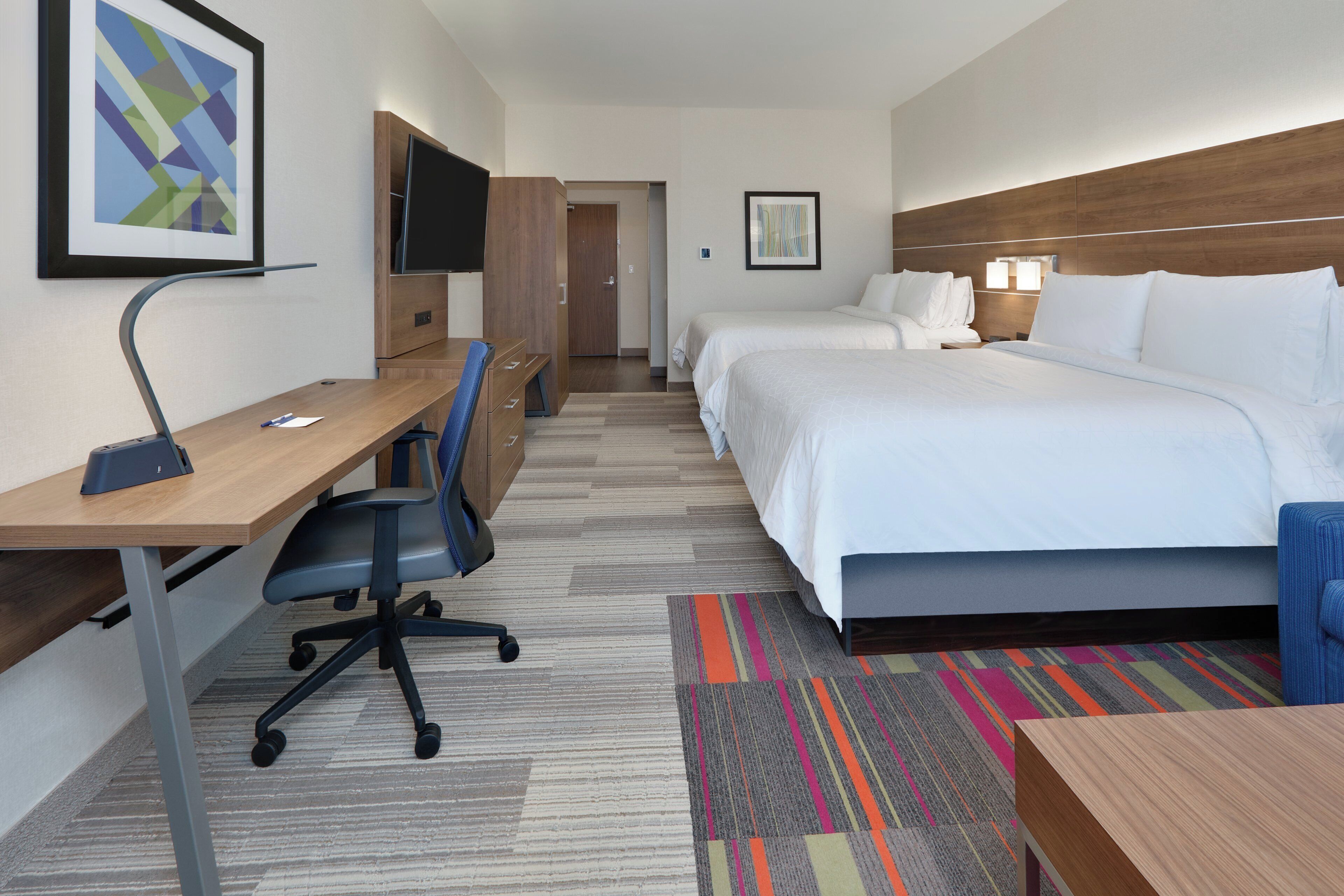 Ein Hotelzimmer mit Bett, Schreibtisch, Stuhl, Fernseher und Kunstwerken.