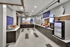 Un área de cocina moderna con una cafetera, un refrigerador con exhibición de yogures y una encimera con diversos alimentos.