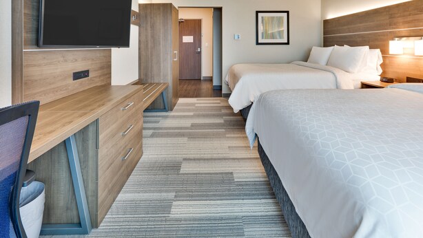 A hotel room with a flat-screen TV, a desk with drawers, two beds with white bedding, and a patterned carpet. - Holiday Inn Express & Suites Plano East - Richardson by IHG (Plano)