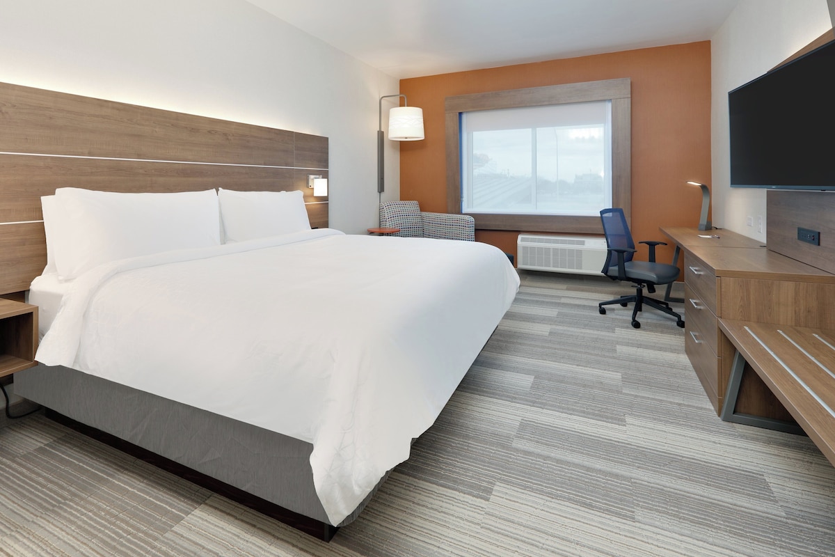 A hotel room with a large bed, a desk with a chair, a television, and a window with a view.