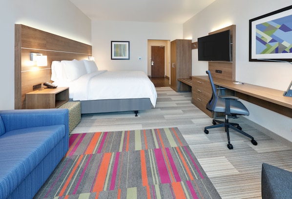 A hotel room with a bed, a desk, a chair, a sofa, a TV, and a bathroom door. - Holiday Inn Express & Suites Plano East - Richardson by IHG (Plano)