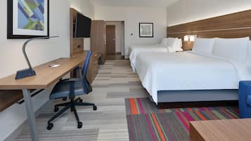 Una habitación de hotel con escritorio, dos camas, un televisor y una alfombra colorida.