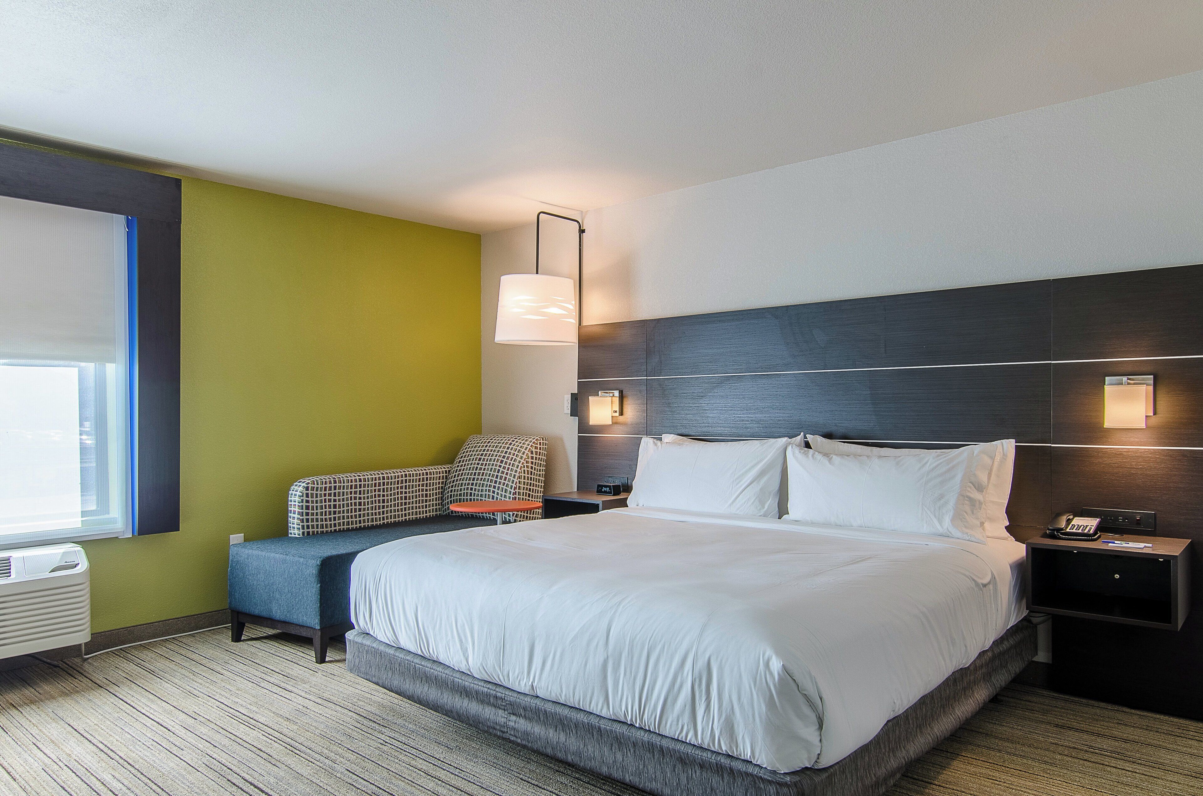 A hotel room with a large bed, a seating area with a patterned sofa, a small table, and a wall-mounted lamp.