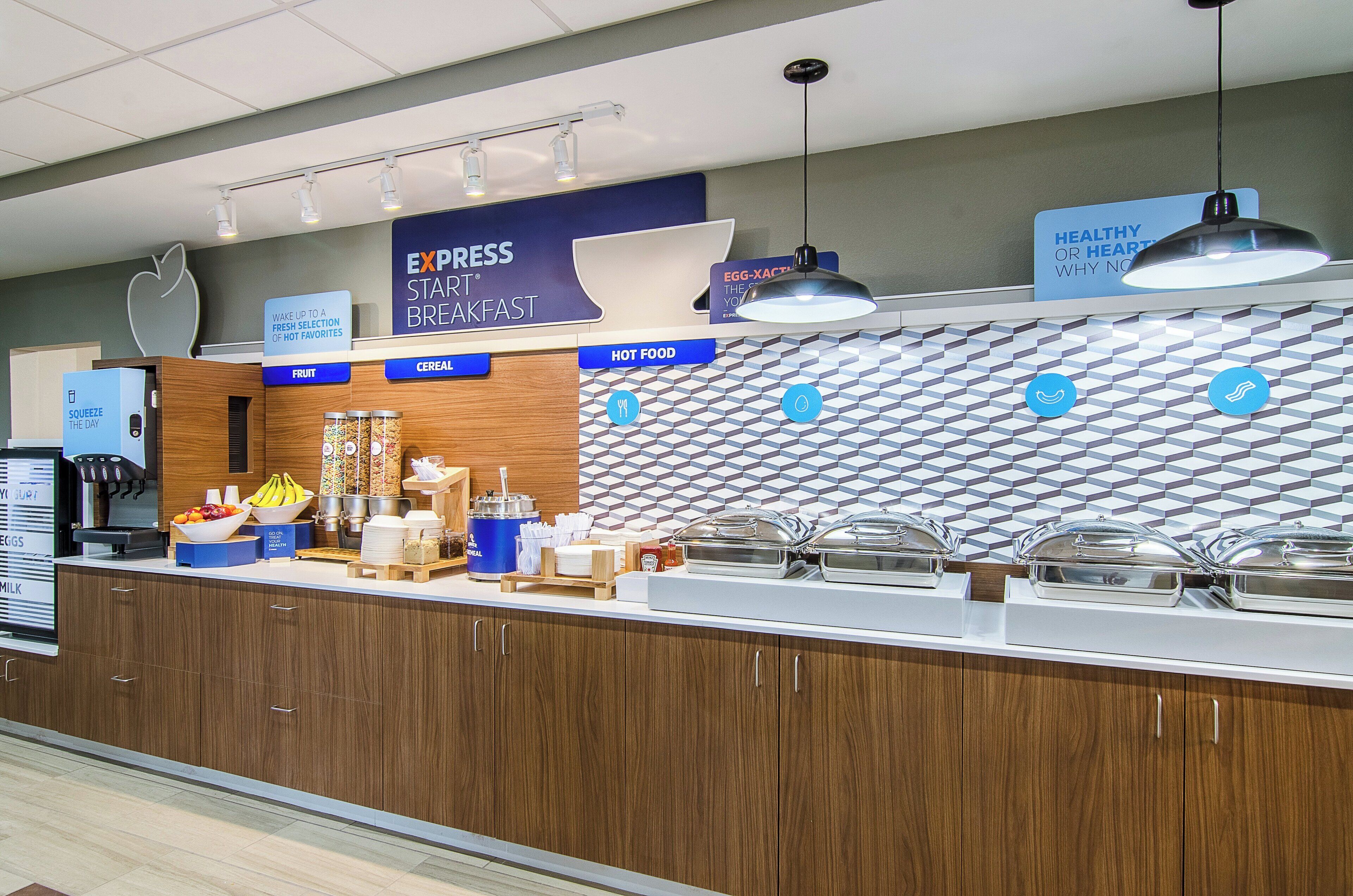Zona de desayuno tipo buffet con secciones identificadas para fruta, cereales y comida caliente, y un letrero para Desayuno Express Start®.