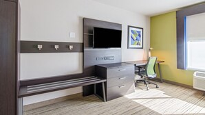 A modern hotel room with a dark wood desk, a flat-screen TV, a green chair, and a window with blinds. - Holiday Inn Express & Suites Atchison by IHG (Atchison)
