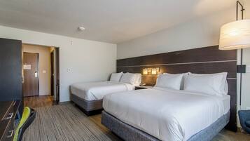 A hotel room with two beds, a desk, a chair, a lamp, and a door.