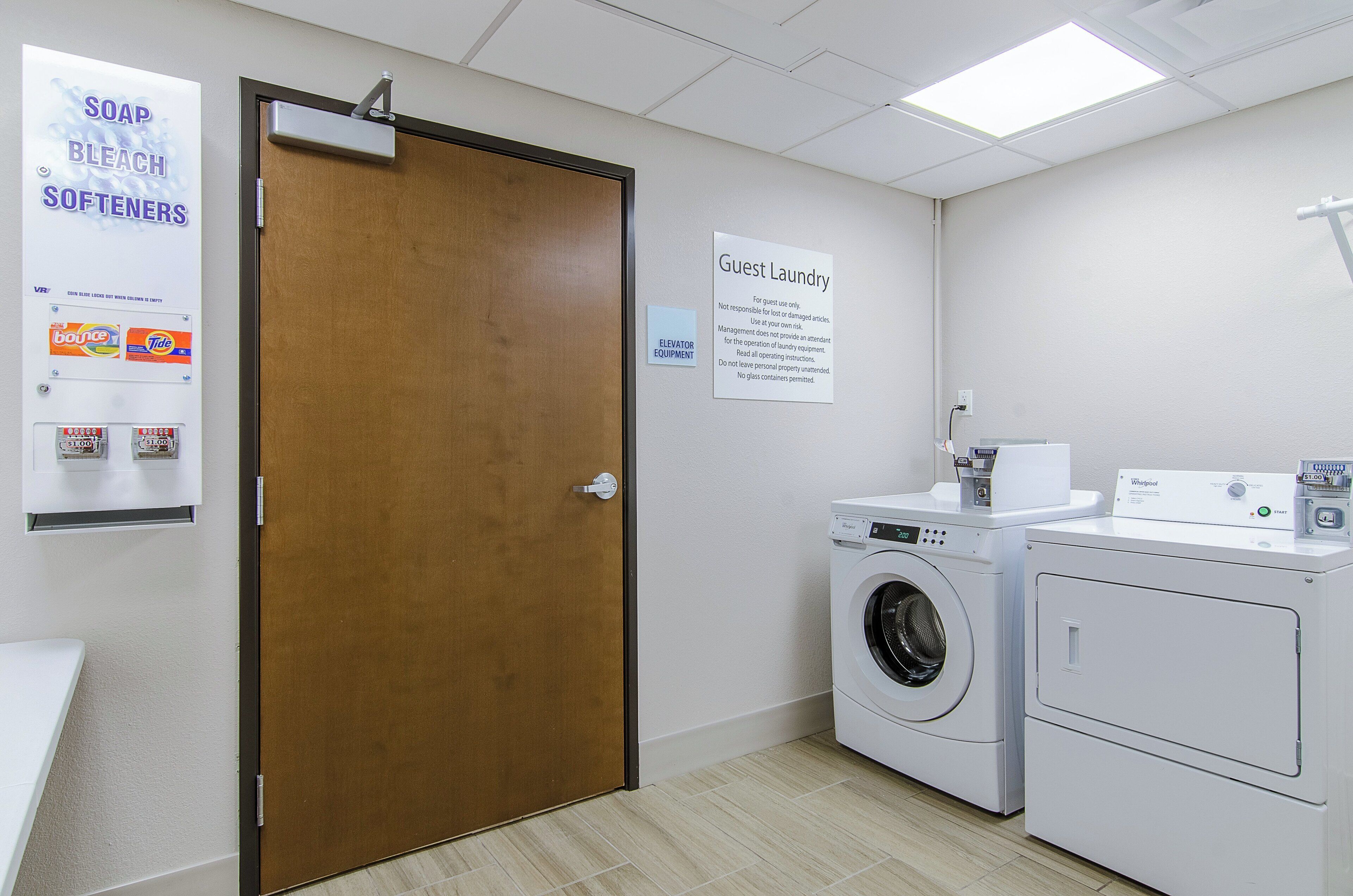 A laundry facility with a door, a sign for guest laundry, and a Whirlpool washer and dryer.