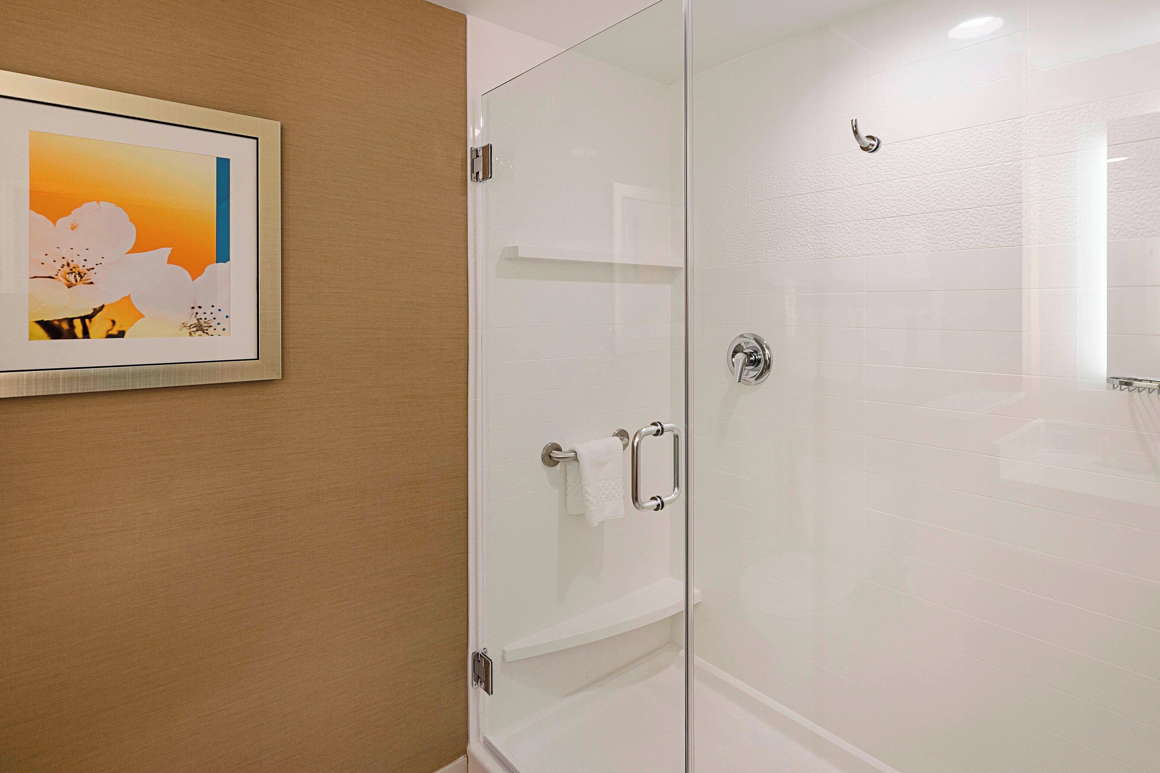 A modern bathroom with a glass shower enclosure, a white towel rack, and a framed picture on the wall.