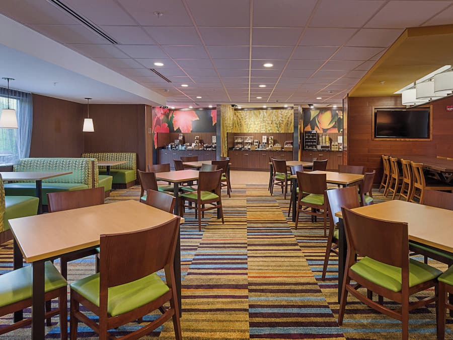A hotel lobby with multiple seating areas, including booths and tables with chairs, a counter with a menu, and a television screen.
