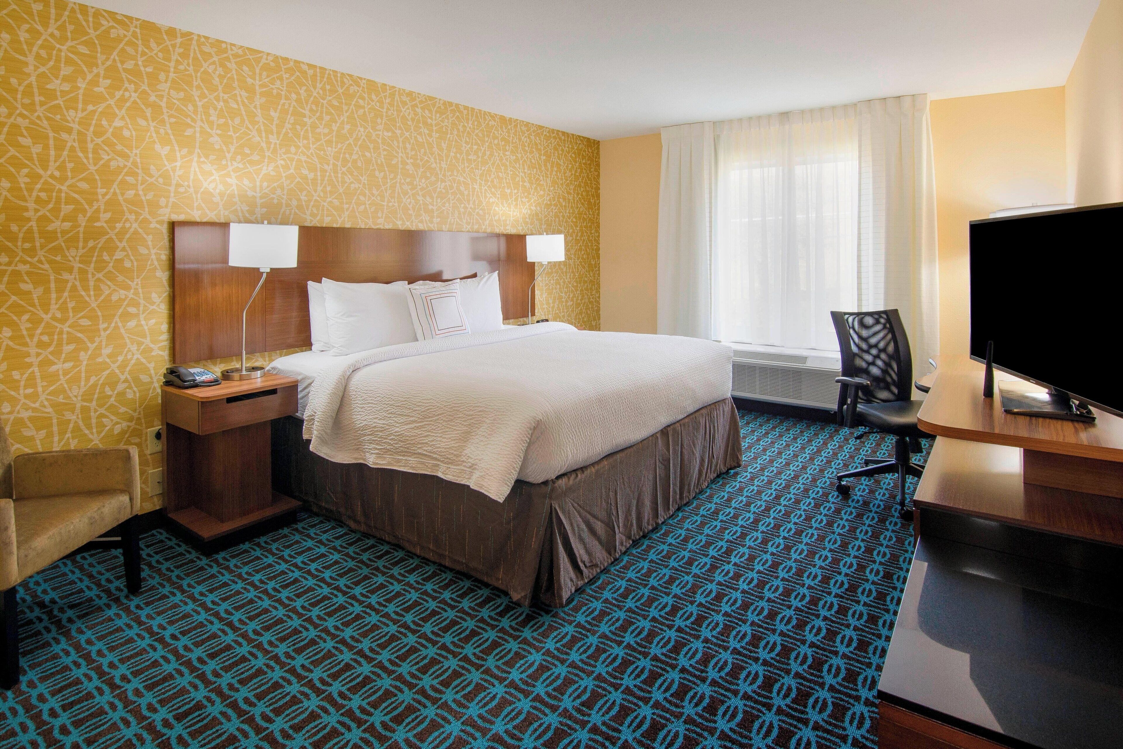 A hotel room with a large bed, a desk with a chair, a television, and a window with curtains.