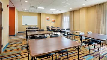Un salón de conferencias con varias mesas y sillas, una pizarra y una pantalla para proyector.