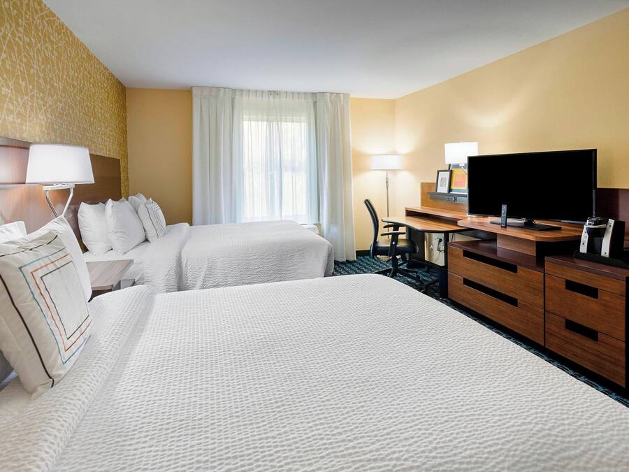 A hotel room with two beds, a desk with a TV, and a dresser.