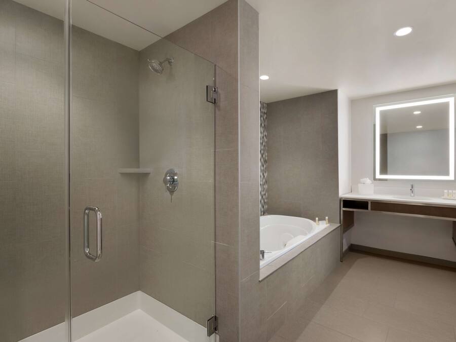 Un baño moderno con ducha de vidrio, una bañera independiente y un tocador con espejo y toallero.