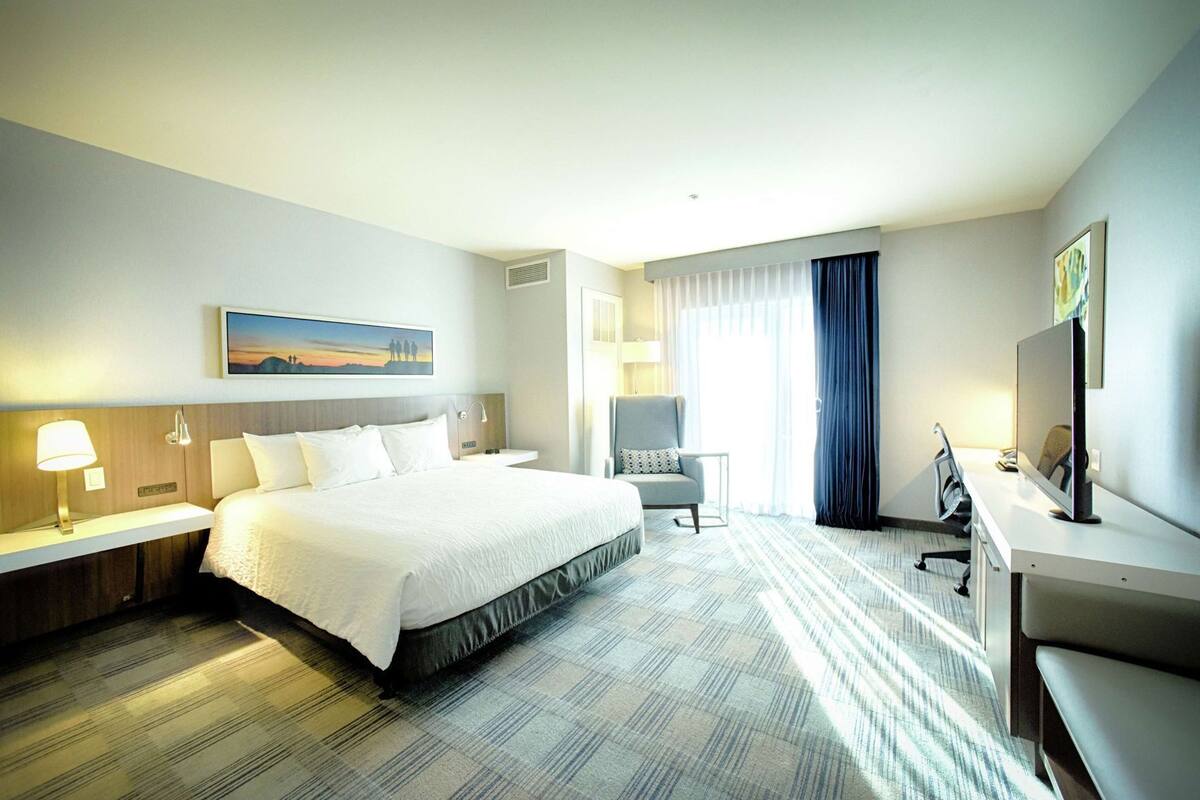 Une chambre d’hôtel avec un grand lit, un bureau avec un ordinateur, une chaise, une lampe et un tableau au mur.