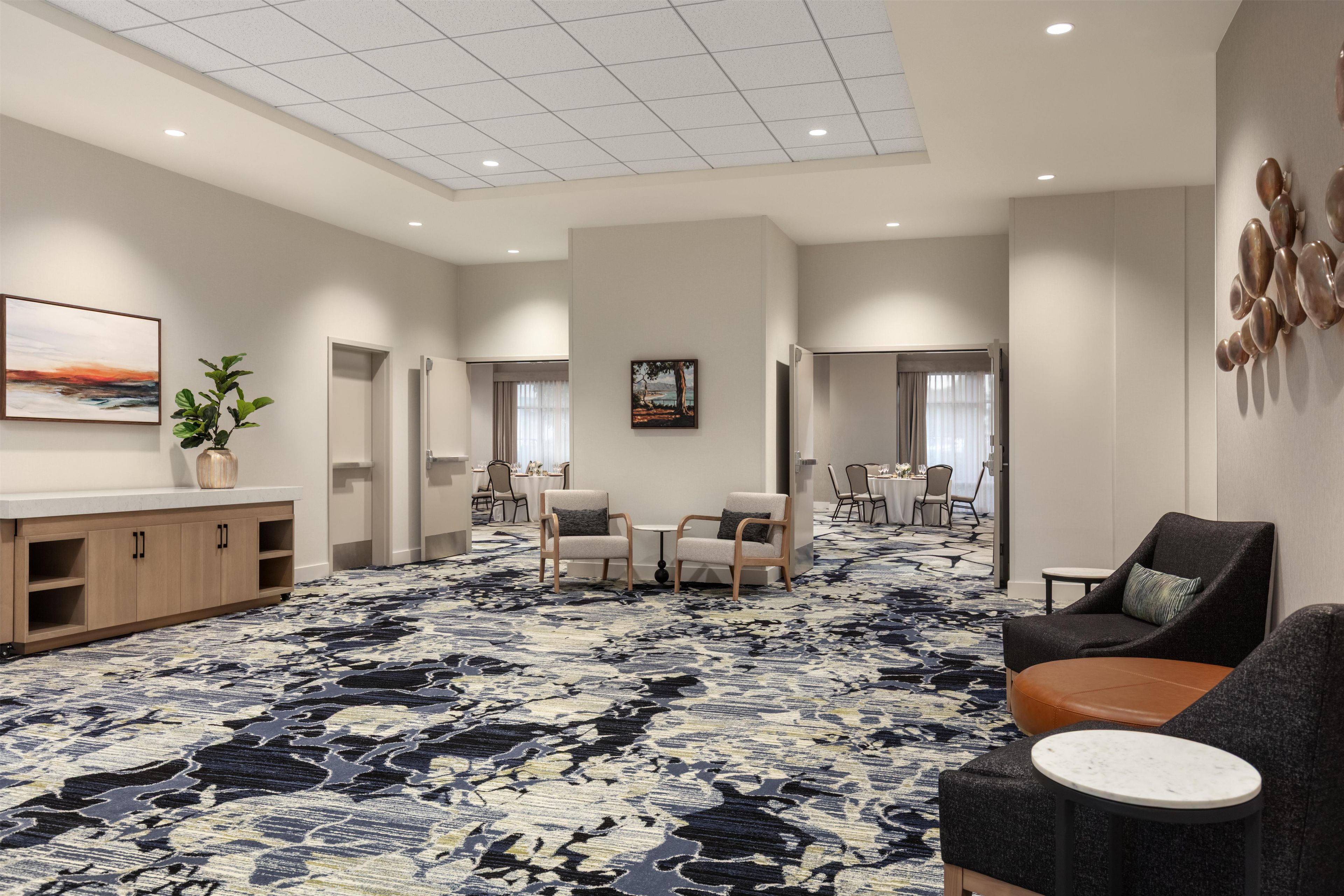 Un vestíbulo de hotel con alfombra estampada, área de descanso, obras de arte y una recepción.