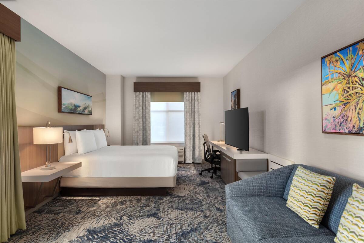 Une chambre d’hôtel avec un lit, un bureau, une télévision et un canapé.
