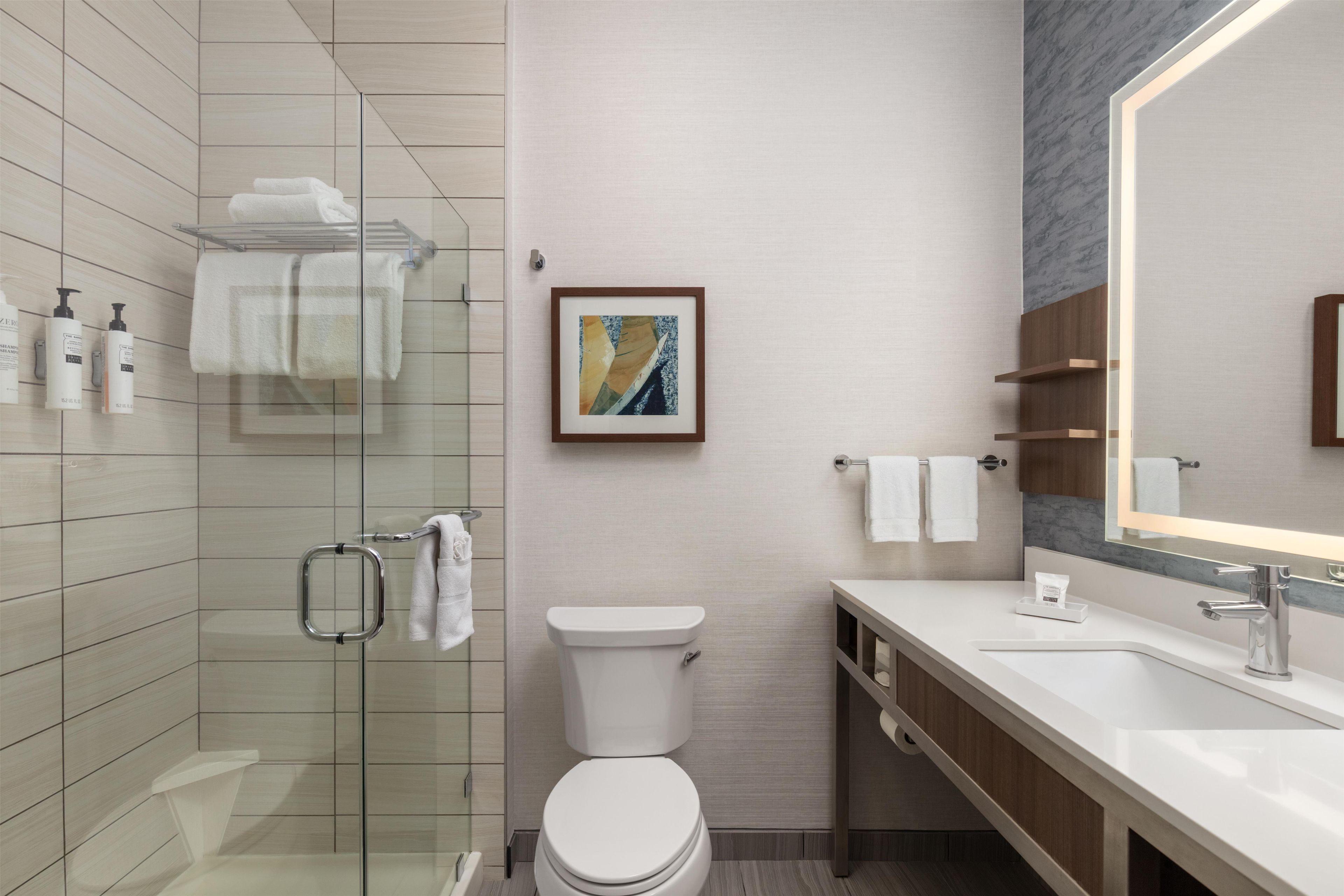 Un baño moderno con cabina de ducha de vidrio, inodoro, lavabo con espejo y una obra de arte enmarcada en la pared.