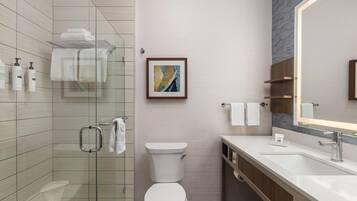 Un baño moderno con cabina de ducha de vidrio, inodoro, lavabo con espejo y una obra de arte enmarcada en la pared.