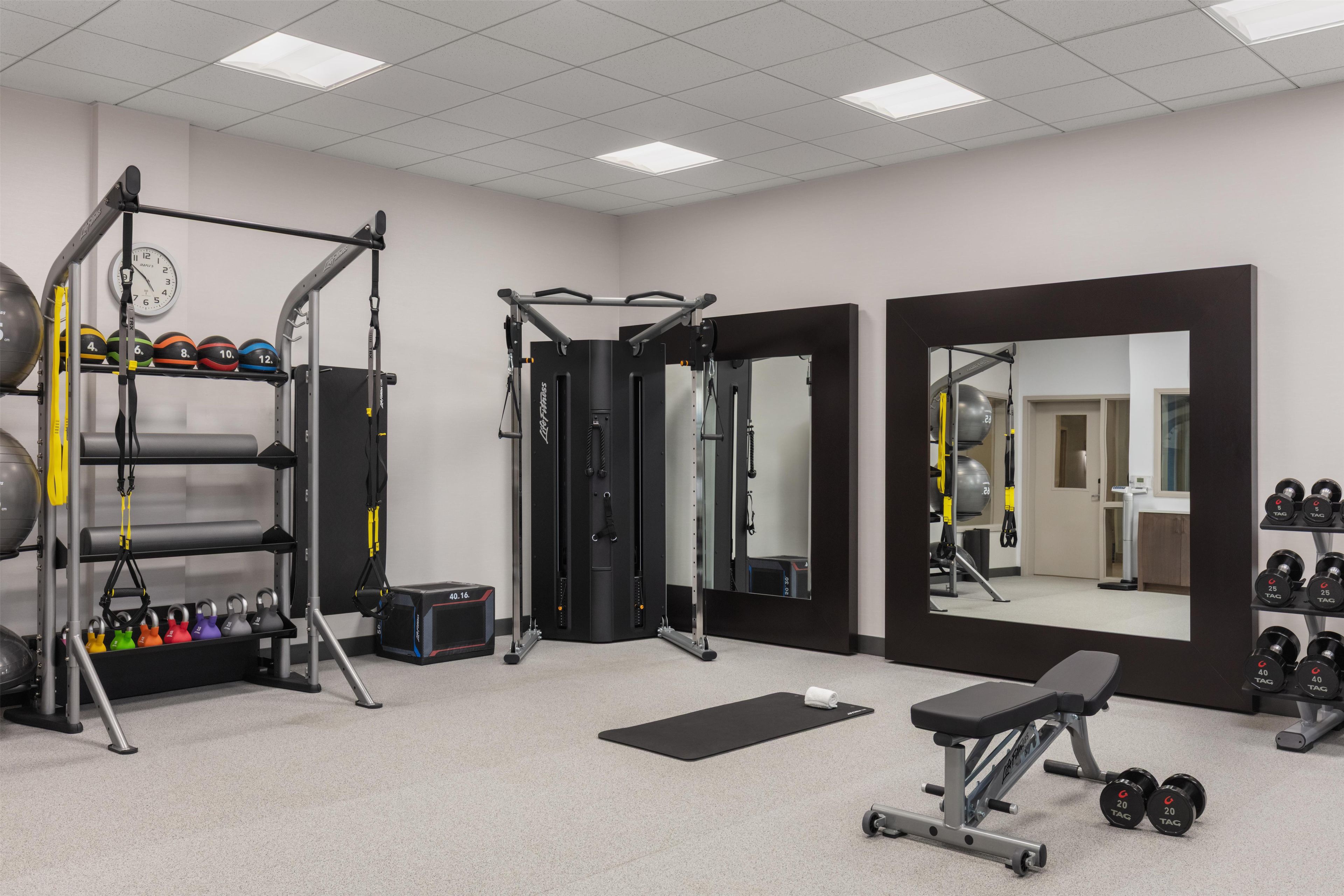 Een sportschool met diverse fitnessapparaten, een spiegel en een bank.