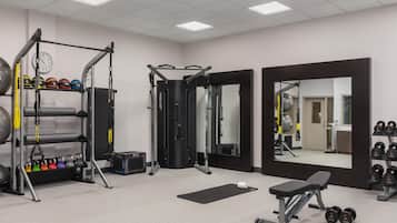 Een sportschool met diverse fitnessapparaten, een spiegel en een bank.