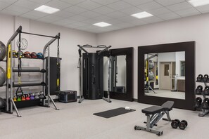 A gym with various exercise equipment, a mirror, and a bench.