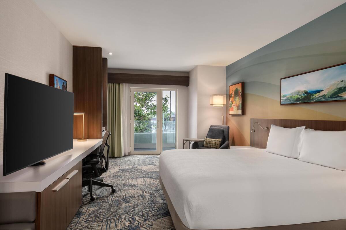 Une chambre d’hôtel avec un lit, un bureau doté d’un téléviseur à écran plat, une chaise, une lampe et un tableau au mur.