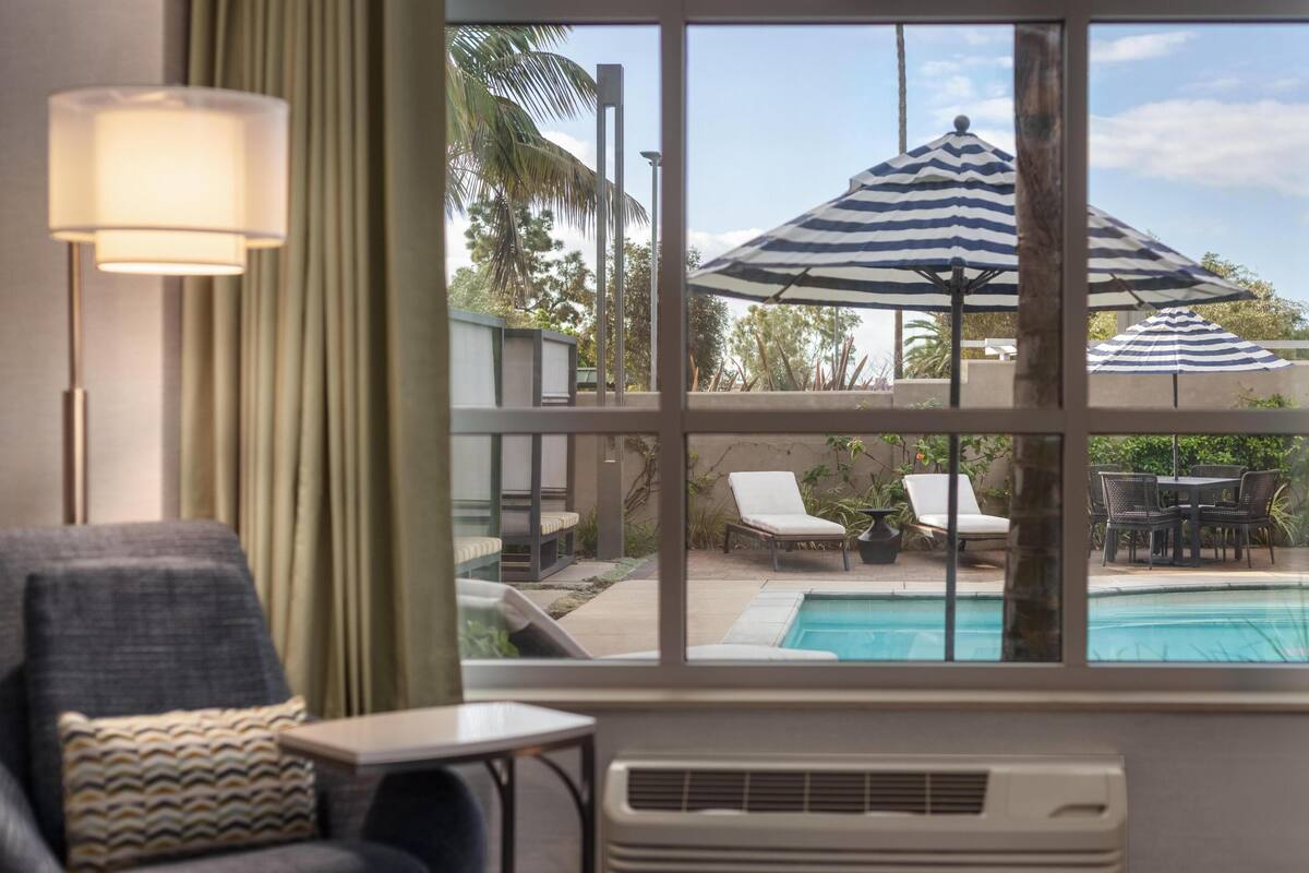 Une chambre avec vue sur une piscine, des chaises longues et un parasol.