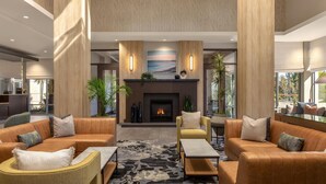 A spacious lobby with leather sofas, a fireplace, and a large window. - Hilton Garden Inn Santa Barbara / Goleta (Goleta)