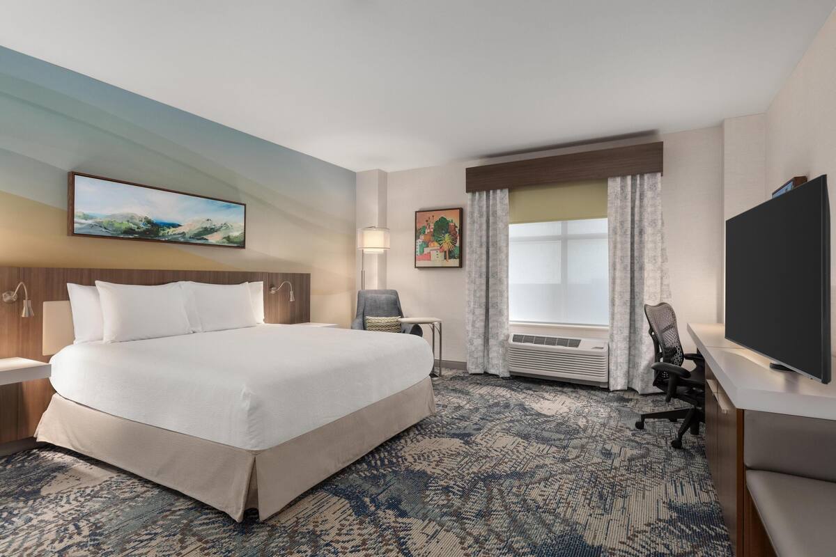 Une chambre d’hôtel avec un grand lit, un bureau, une chaise, une télévision et une fenêtre avec des rideaux.