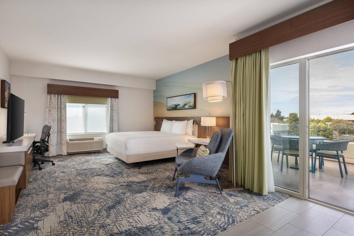Une chambre d’hôtel comprenant un lit, un bureau, une chaise et un balcon avec des sièges d’extérieur.