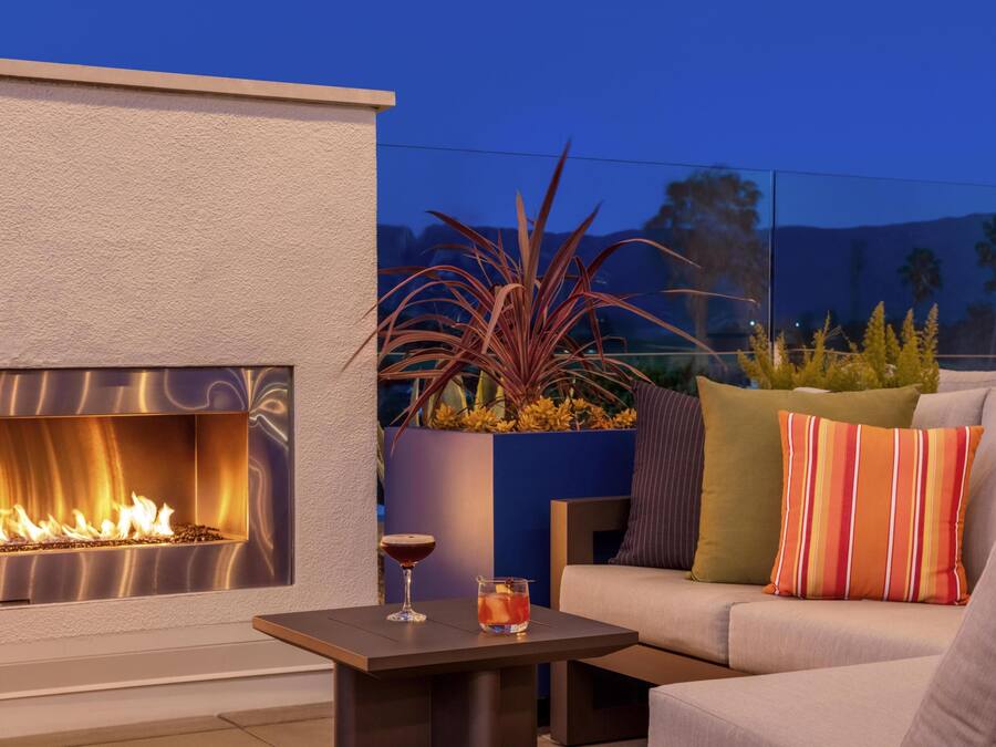 Un área de estar exterior moderna con una chimenea, una mesa de vidrio y un sofá con cojines a rayas.