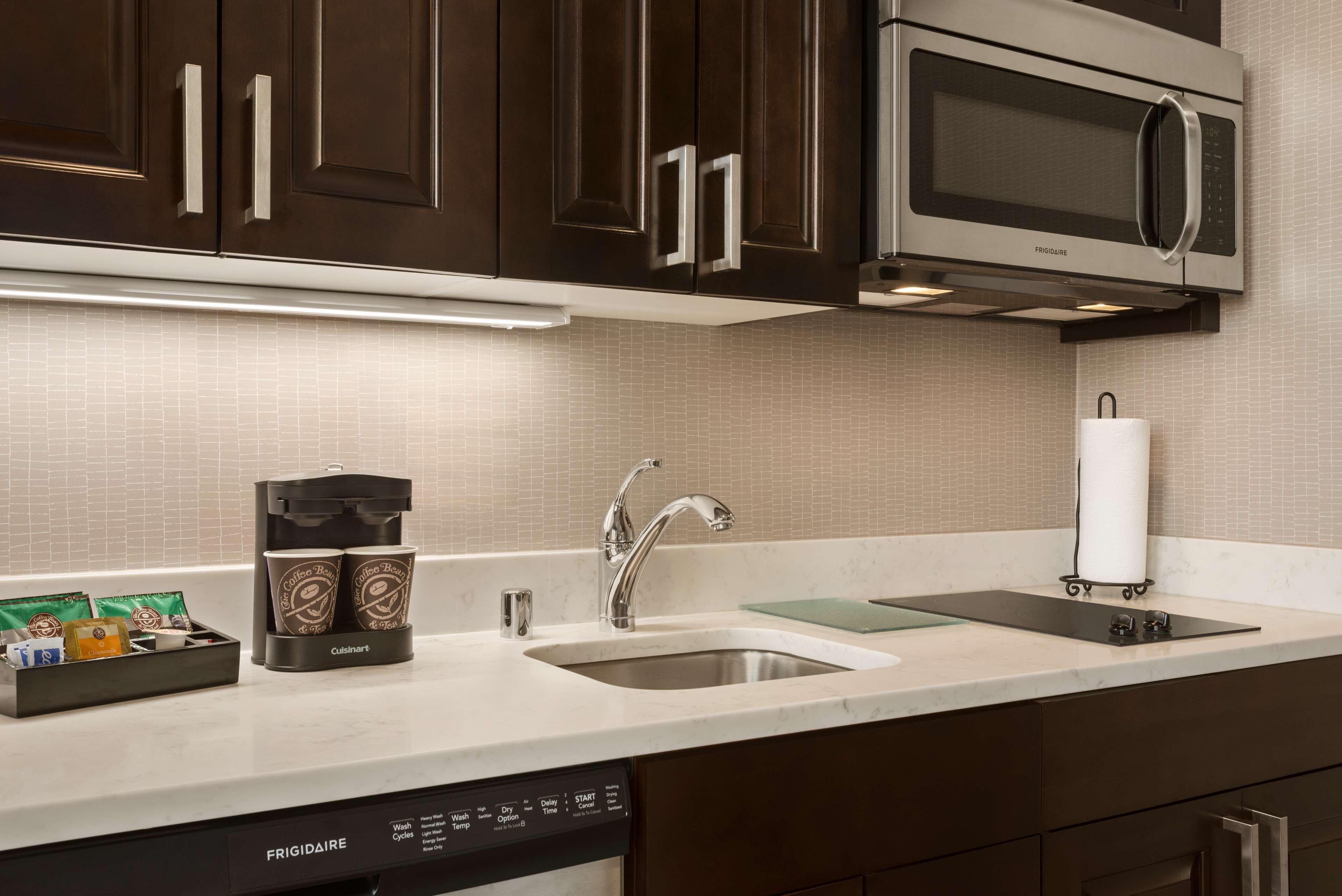 A kitchen with dark brown cabinets, a stainless steel microwave, a coffee maker, and a dishwasher.