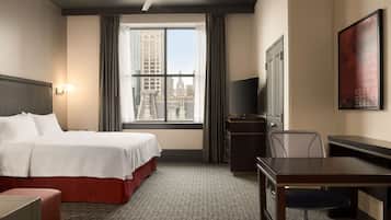 Quarto de hotel com cama, escrivaninha, cadeira, televisão e janela com vista para a cidade.