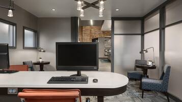 A modern office space with a large desk, computer, and ergonomic chair. There are multiple tables with lamps, a large window, and a brick wall.