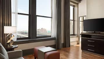 A hotel room with a large window, a TV, a sofa, a small table, and a cabinet.