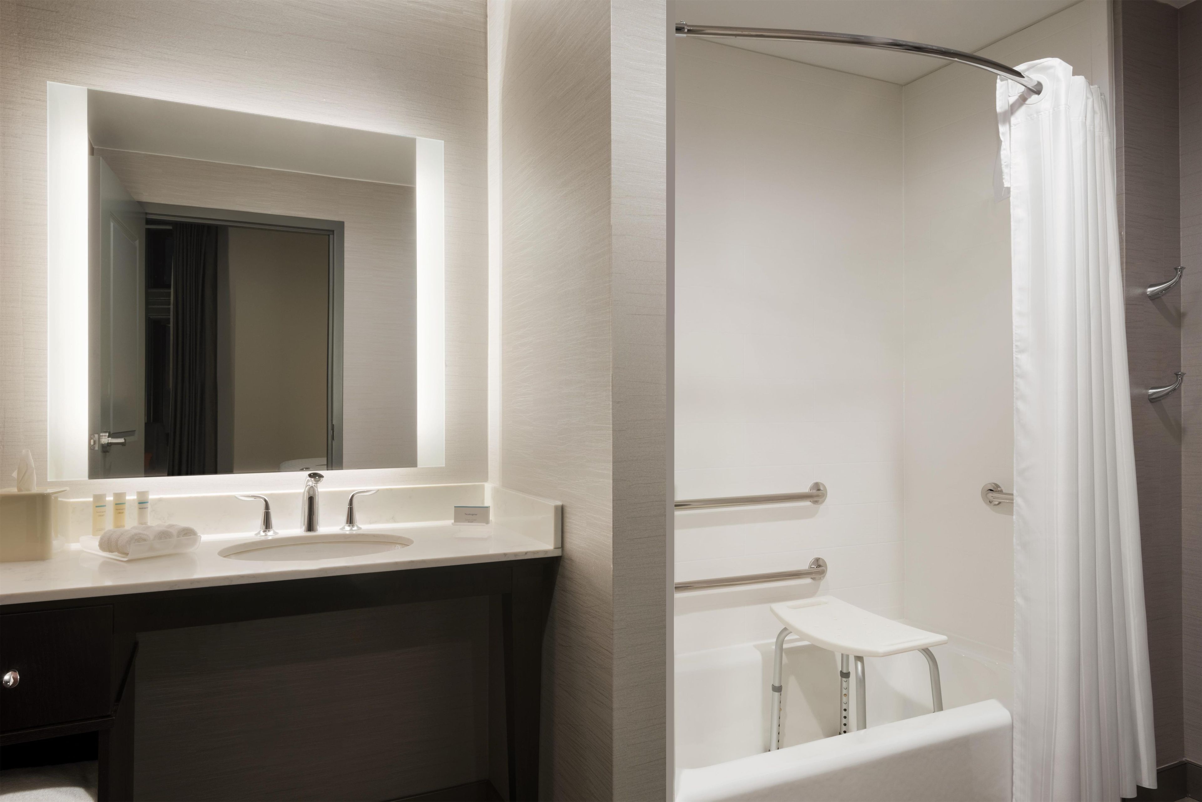 A modern bathroom with a large mirror, a sink, a vanity, and a shower area.