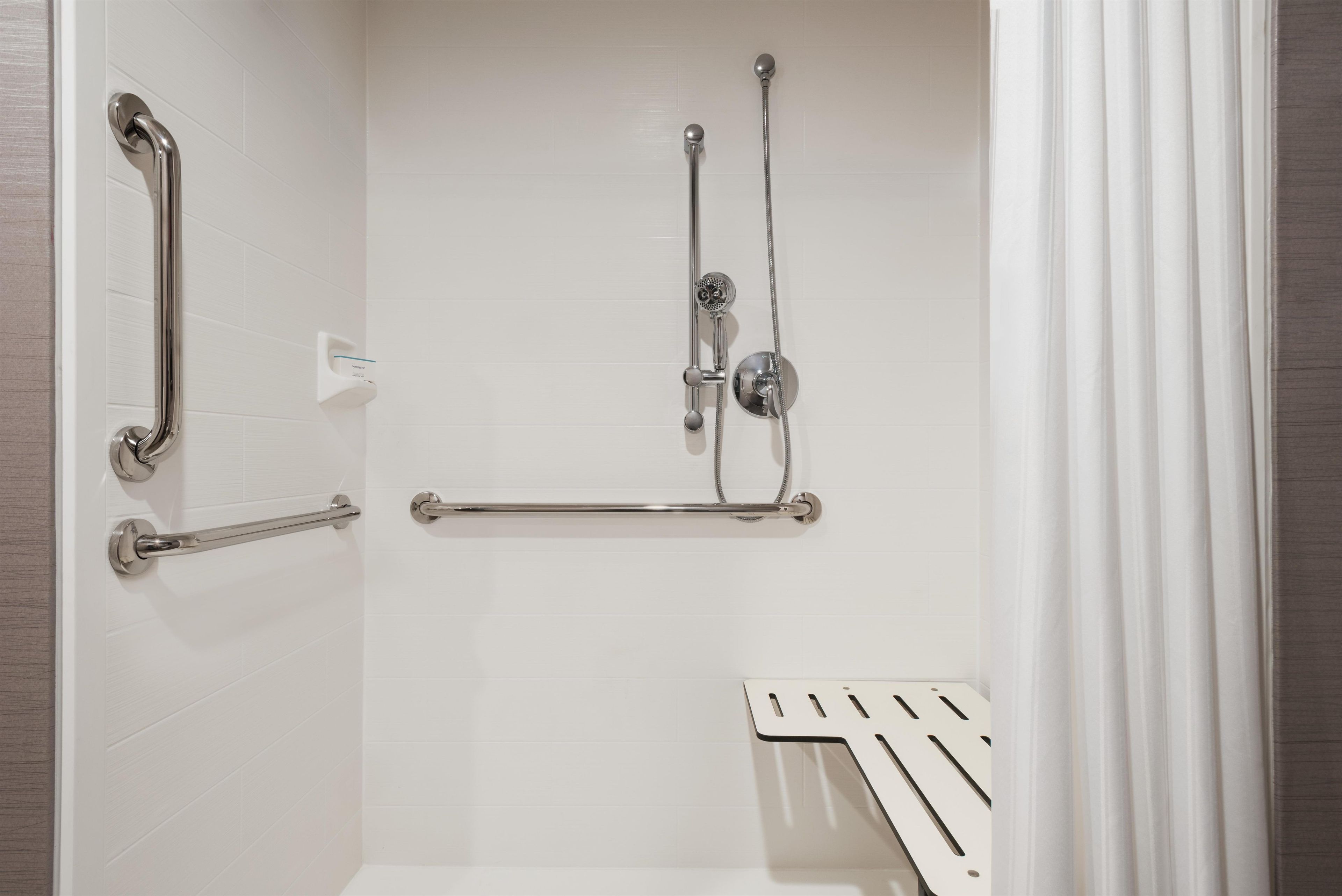 Un espace douche équipé d’une barre d’appui, d’un pommeau de douche à main et d’un flexible de douche.