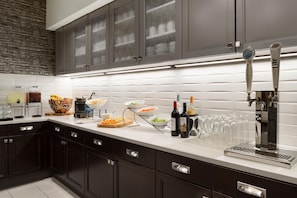 Una cocina moderna con armarios oscuros, encimera blanca y una variedad de alimentos y bebidas.