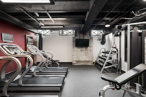 A gym with treadmills, a weight bench, and a TV screen.