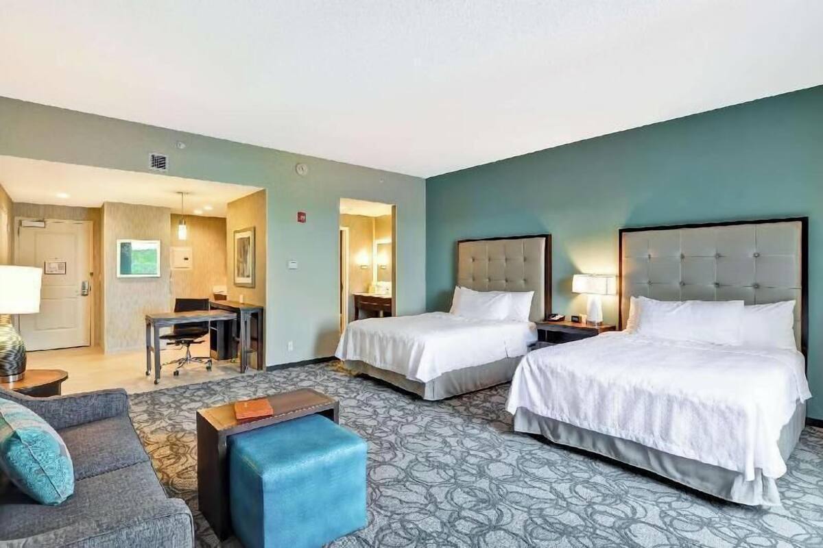 A hotel room with two beds, a desk, a sofa, and a patterned carpet.