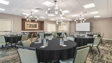 A conference room with round tables, chairs, water bottles, a projector screen, and a large mirror.