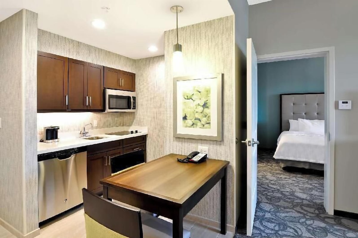 A compact hotel room with a kitchenette, a dining area, and a bed.