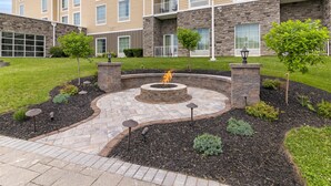 A courtyard with a fire pit, stone benches, and small trees. - Homewood Suites By Hilton Schenectady (Schenectady)
