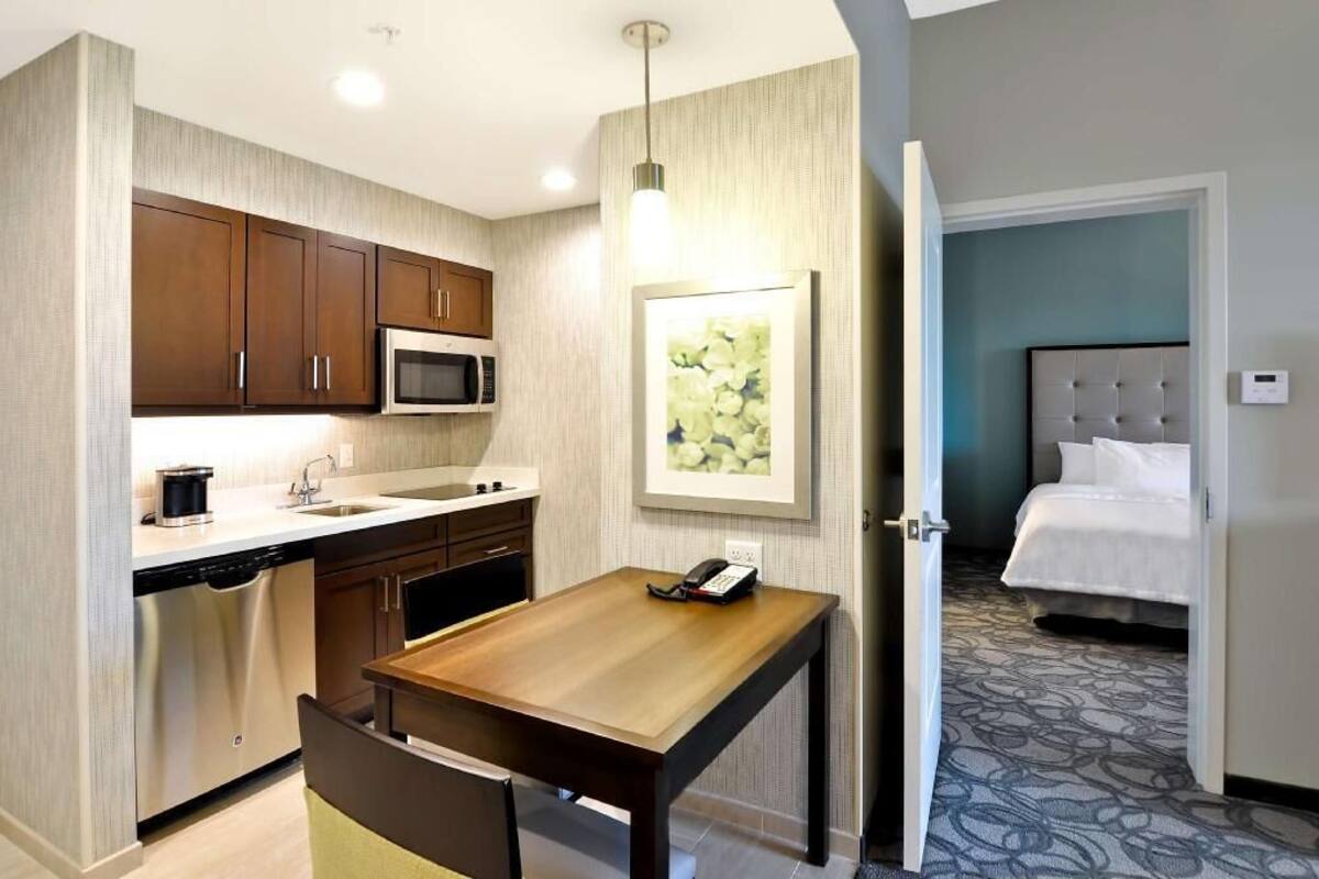 A compact hotel room with a kitchenette, a dining area, and a bed.