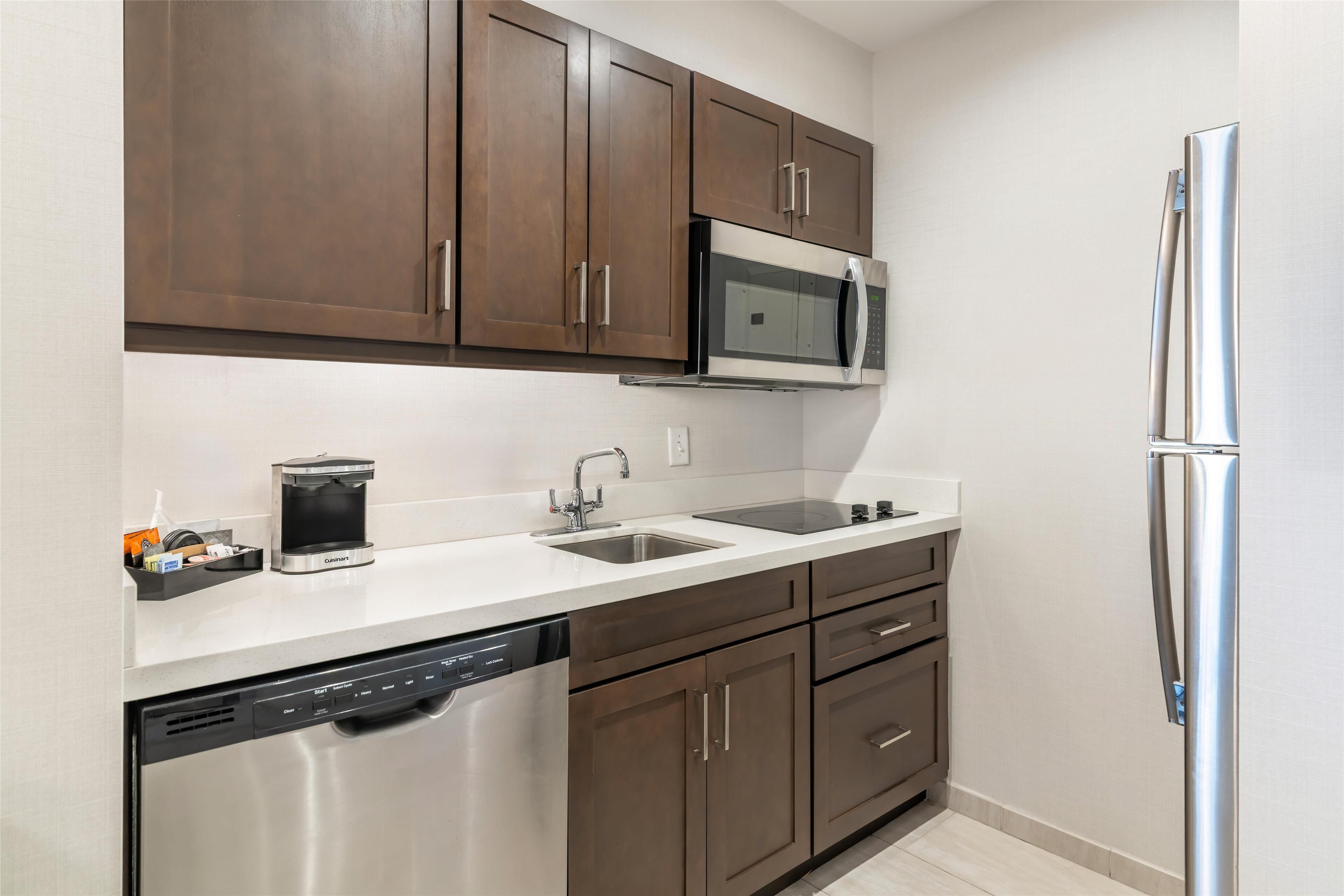 A modern kitchen with stainless steel appliances, a dishwasher, and brown cabinetry.