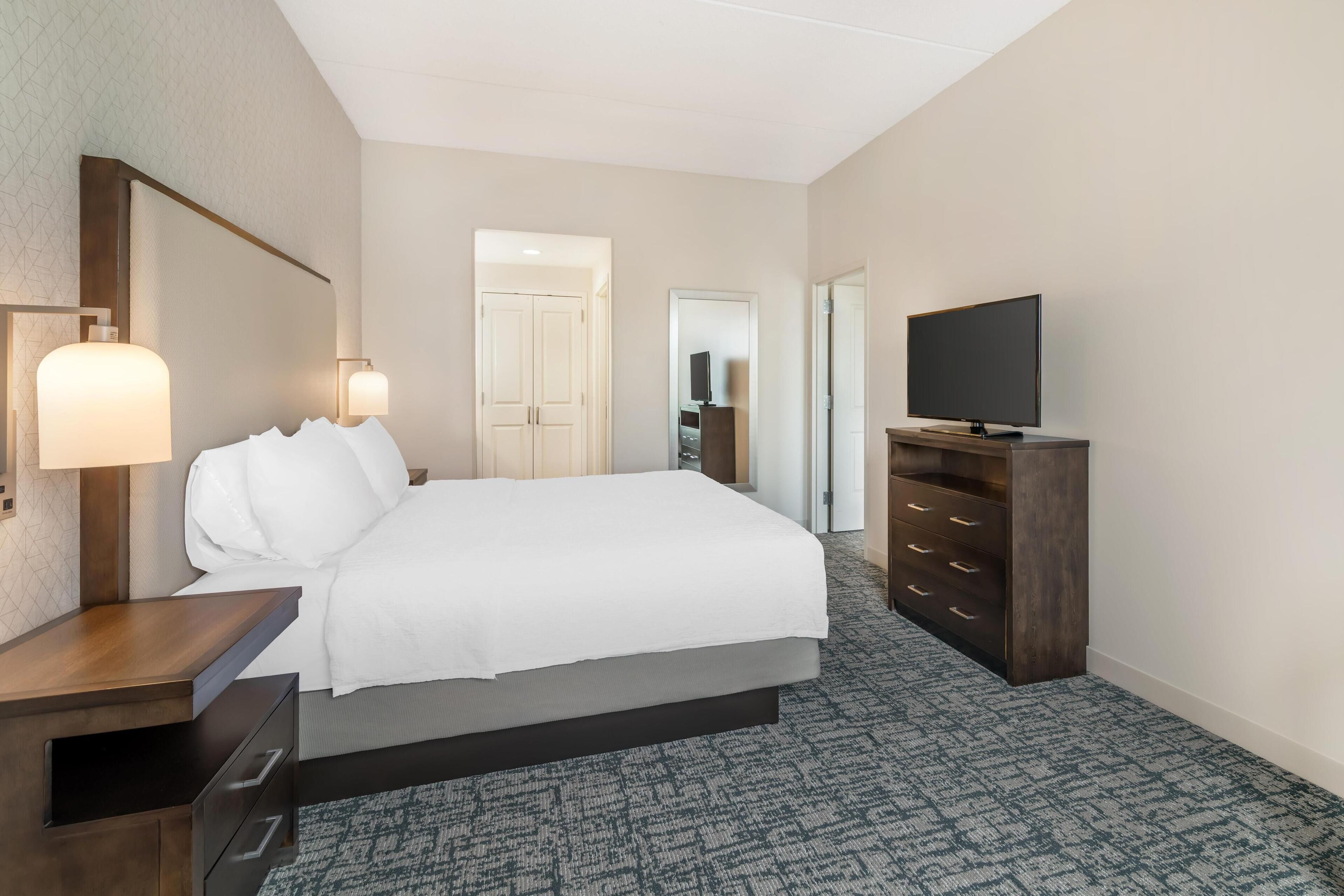A hotel room with a bed, bedside table, TV, and a dresser.